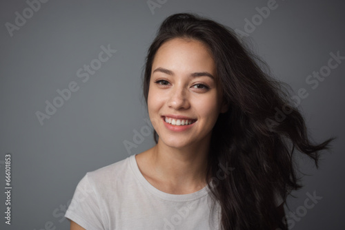Everyday people. A happy asian woman laughing. Black windswept wavy hair to her shoulders. Wearing a white shirt. Pretty woman. University student. Wholesome. On a grey studio background. Portrait. © Delta Amphule