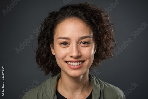 Everyday people. A smiling european woman. Brown curly hair to her shoulders. Wearing a shirt. On a dark grey studio background. Portrait.