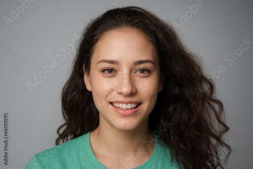 Everyday people. A smiling European student. Brown wavy hair over her shoulder. Wearing a white sleeveless shirt. On a light studio background. Portrait. 