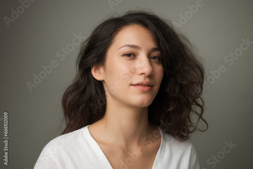 Everyday people. A serious woman. Brown shoulder length wavy hair. Wearing a light shirt. Cautious. Introspective. University student. On a light studio background. Portrait.