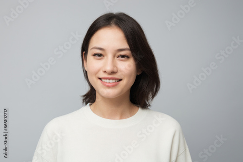 Everyday people. A smiling asian woman. Brown straight hair to her shoulders. Hair volume. Wearing a white shirt. On a light studio background. Portrait.