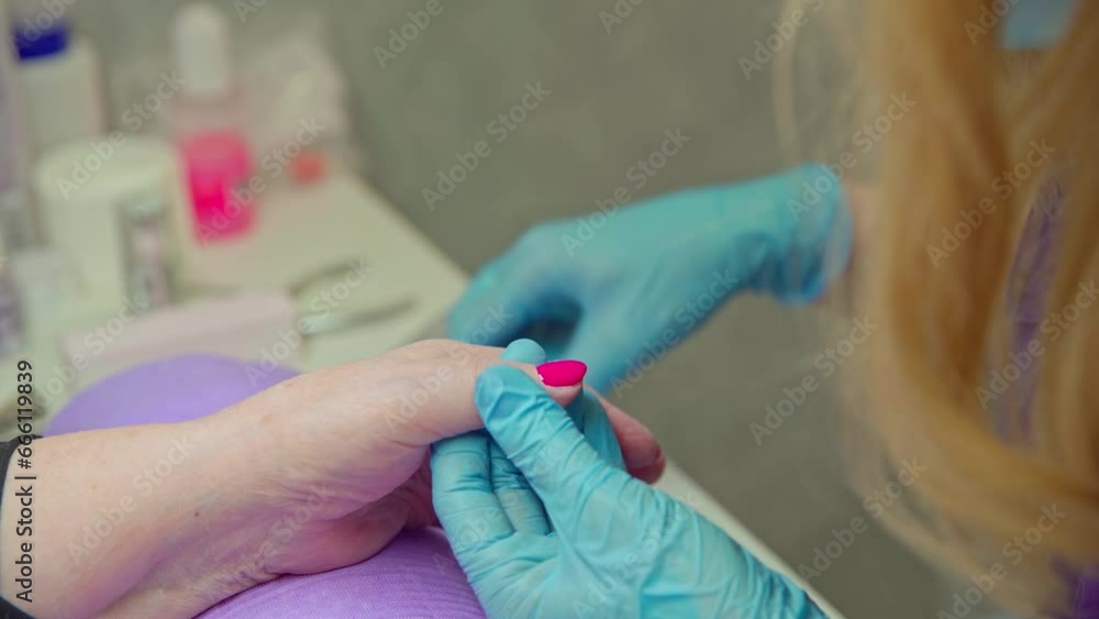 Manicurist precisely paints client's nails a deep pink color Manicurist precisely paints client's nails a deep pink color