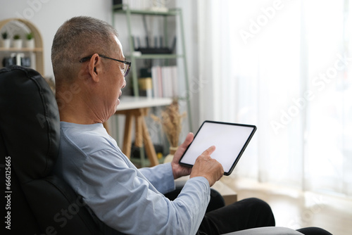 Senior Asian men at the sofa couch using smartphone tablet for browsing internet and reading news online in the morning. photo