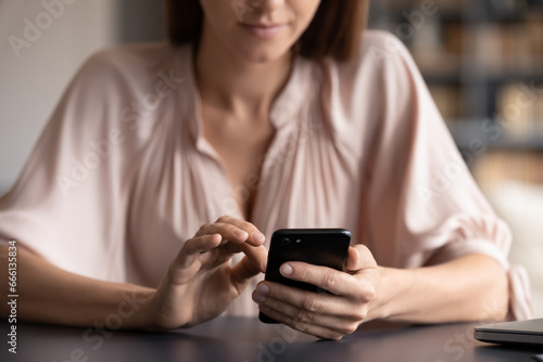 Woman sit at table indoors close up view focus of female hands holds black smart phone, e-dating usage, user of easy convenient on-line services, e-commerce, webshop buyer, websurfing activity concept