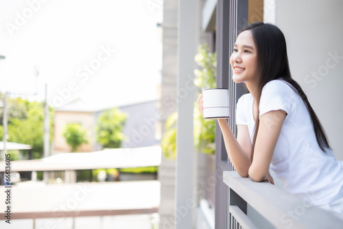Young Asian beautiful woman drinking coffee and looking away with snile of happiness in the moring, freshness moment for starting in morning. photo