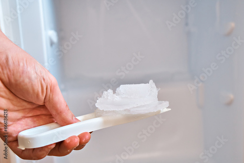 A man holds a shovel with ice on the background of a freezer. Defrosting the freezer. photo