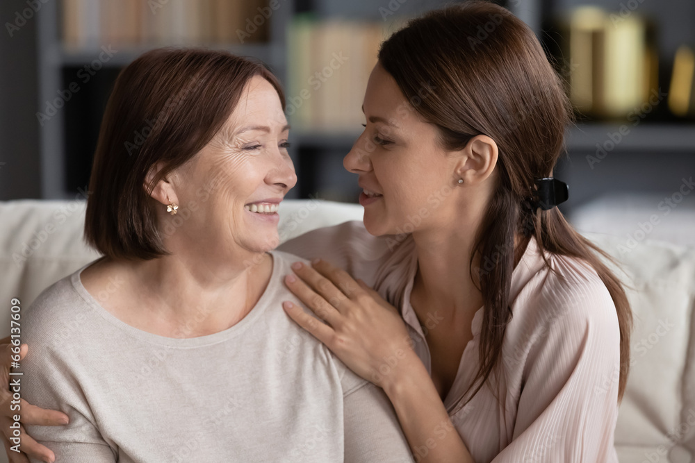 Naklejka premium Close up beautiful adult daughter hugs lovely aged mother loving women different generations relatives females sit on couch looking at each other feels happy spend time together, love and care concept