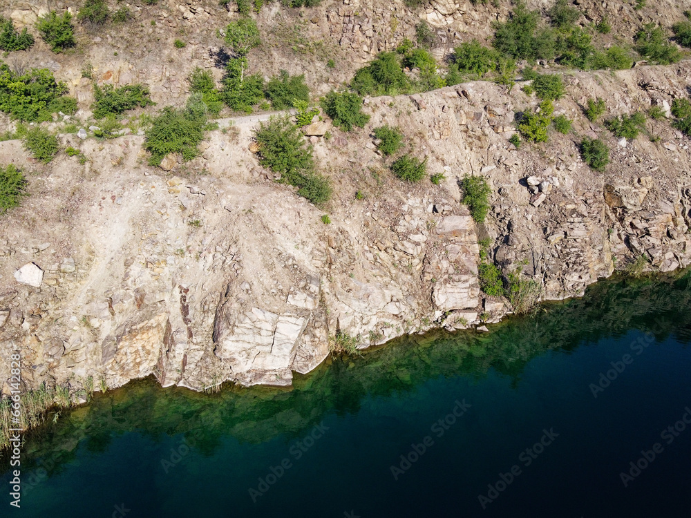 Rocky shore of the Radon Lake on a sunny summer morning. Aerial view of an old flooded granite quarry. A picturesque pond.