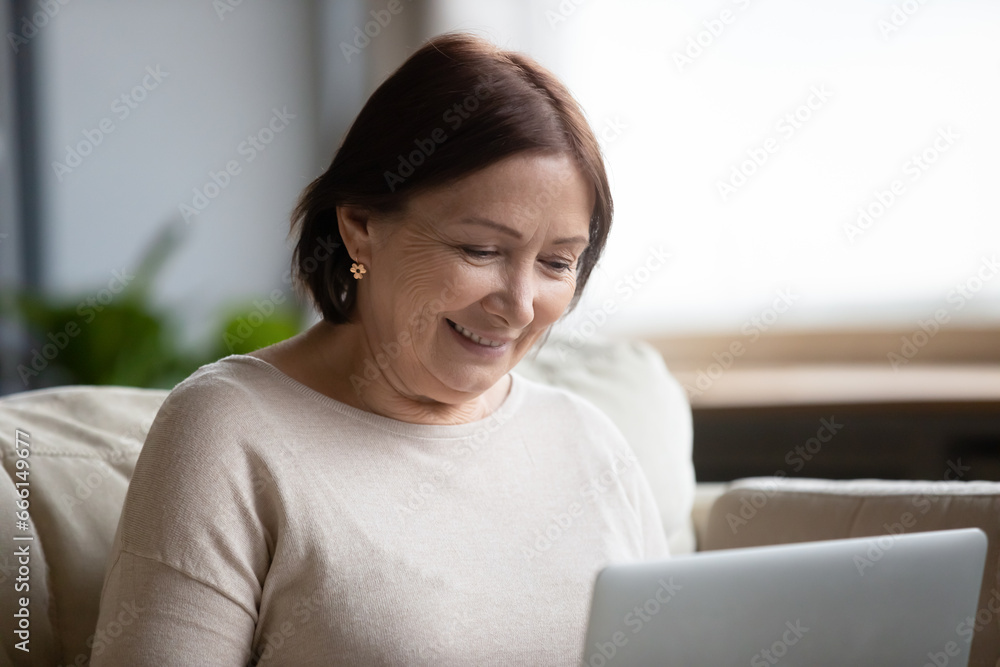 Elderly 60s woman sit on sofa holds laptop feels comfortable using modern tech, surfing website search useful info enjoy personal development, older generation and device easy convenient usage concept Elderly 60s woman sit on sofa holds laptop feels comfortable using modern tech, surfing website search useful info enjoy personal development, older generation and device easy convenient usage concept