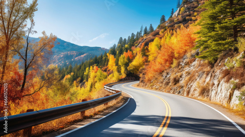 A winding mountain road with colorful fall foliage and a clear blue sky