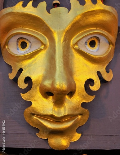A golden mask with big eyes, long nose, thin lips and cheeks and forehead in curvy designs,