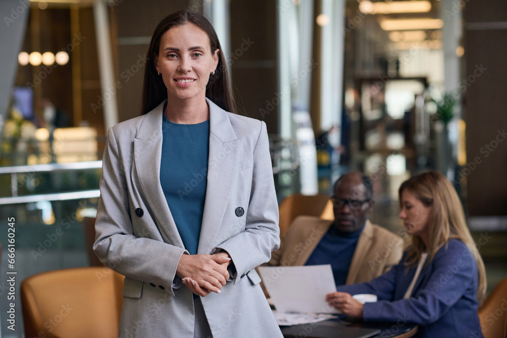 Portrait of businesswoman smiling at camera while having meeting with her colleagues in the hotel Portrait of businesswoman smiling at camera while having meeting with her colleagues in the hotel