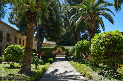 View of a rest plaza with palm trees and vegetation with a stone and cement hallway and a statue at the end of it