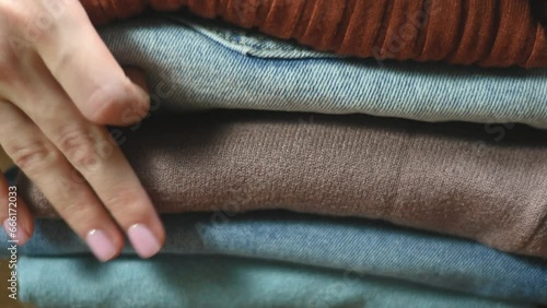 Woman folds clothes, jeans, warm sweaters into a pile stack on blur background