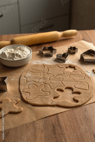 Holiday concept. Home baking concept.
Step by step process for making homemade cookies. A layer of dough with New Year's themed cookie figures on a wooden kitchen table.