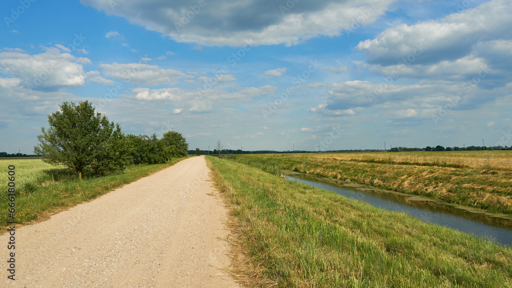 irrigation canal along a field and an empty dirt road. Reclamation channel for improving hydrological, soil and agro-climatic conditions in order to increase the efficiency of land