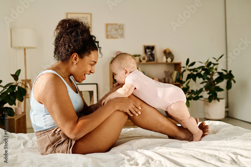 Happy mother sitting on bed and playing with her child at home
