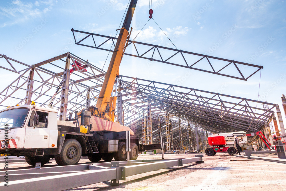Installation of metal rafter trusses of the covered warehouse with a car crane. Metall frame storage building Installation of metal rafter trusses of the covered warehouse with a car crane. Metall frame storage building