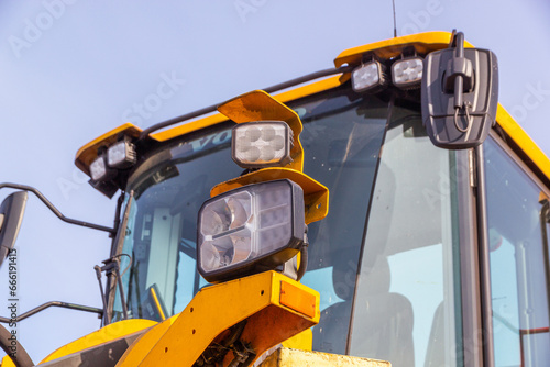 Close up view of the big yellow tractor. Headlight of the front end loader