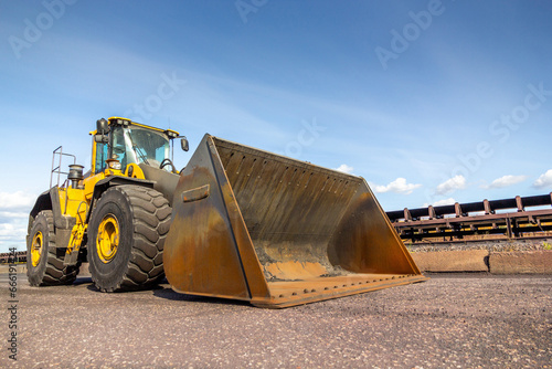 Heavy duty yellow tractor on the road near belt conveyor. Front End Loader