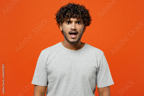 Canvas Print Young sad shocked astonished scared fearful Indian man he wearing t-shirt casual clothes looking camera with opened mouth isolated on orange red color background studio portrait