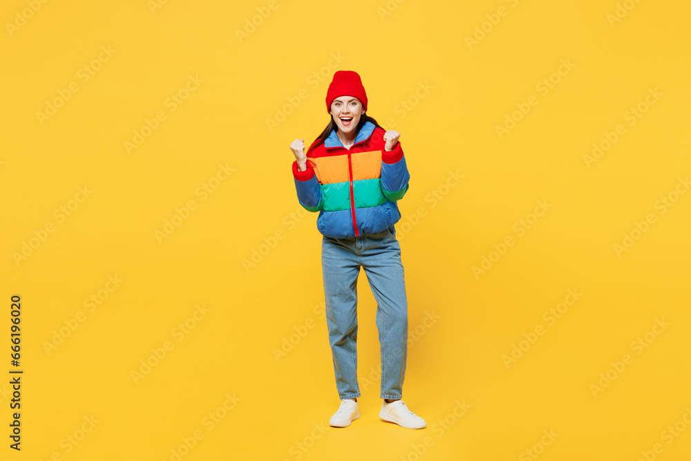 Full body young woman she wears padded windbreaker jacket red hat casual clothes doing winner gesture celebrate clenching fists say yes isolated on plain yellow background studio. Lifestyle concept. Full body young woman she wears padded windbreaker jacket red hat casual clothes doing winner gesture celebrate clenching fists say yes isolated on plain yellow background studio. Lifestyle concept.