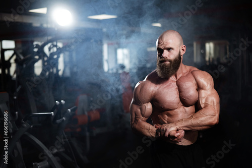Muscular bald man posing shirtless. Bodybuilder showing off his shape in the gym. 