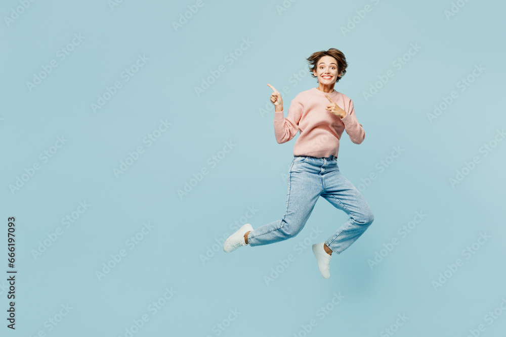 Full body side view young happy woman she wear beige knitted sweater casual clothes jump high point index finger aside on area isolated on plain pastel light blue cyan background. Lifestyle concept.