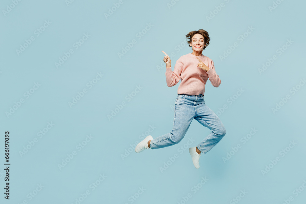 Full body side view young happy woman she wear beige knitted sweater casual clothes jump high point index finger aside on area isolated on plain pastel light blue cyan background. Lifestyle concept. Full body side view young happy woman she wear beige knitted sweater casual clothes jump high point index finger aside on area isolated on plain pastel light blue cyan background. Lifestyle concept.