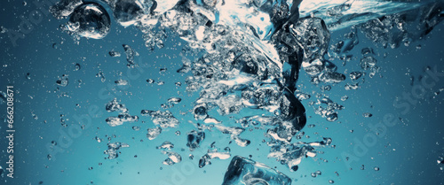 Water splashing and ice cube. Ice splashing into a glass of water. Underwater pouring ice cubes falling into clear watering background. Refreshing chill drinking. Ices in a glass with blue background