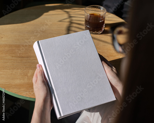 Εκτύπωση καμβά Book cover mock up, hand holding blank clean hardback mockup on wooden desk