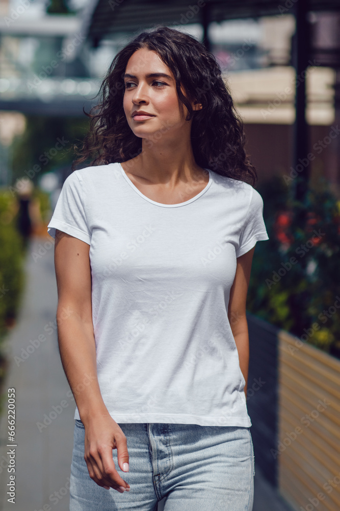 Attractive brunette woman with curly hair in a white t-shirt walks on the street. Attractive brunette woman with curly hair in a white t-shirt walks on the street.