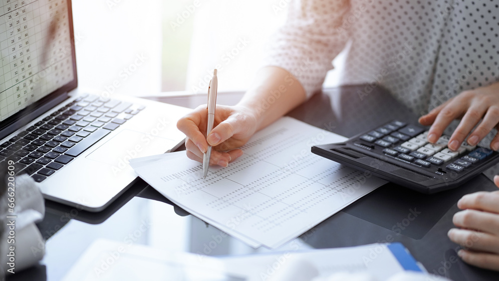 Woman accountant using a calculator and laptop computer while counting taxes for a client. Business audit concepts Woman accountant using a calculator and laptop computer while counting taxes for a client. Business audit concepts