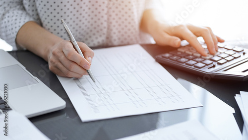 Woman accountant using a calculator and laptop computer while counting taxes for a client. Business audit concepts