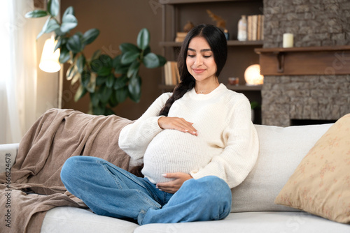 Obraz na płótnie Pregnancy with beautiful pregnant woman hugging her belly sitting on the couch at home. Happy pregnancy with sweet Indian mommy-to-be. w salonie