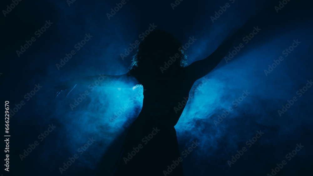 Female dancer. Professional choreography. Emotional graceful woman artist silhouette moving in haze shadow projector light dark blue background copy space.