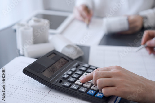 Two accountants use a calculator and laptop computer for counting taxes or revenue balance. Business, audit, and taxes concepts © rogerphoto