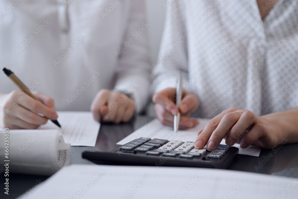 Two accountants use a calculator and laptop computer for counting taxes or revenue balance. Business, audit, and taxes concepts Two accountants use a calculator and laptop computer for counting taxes or revenue balance. Business, audit, and taxes concepts