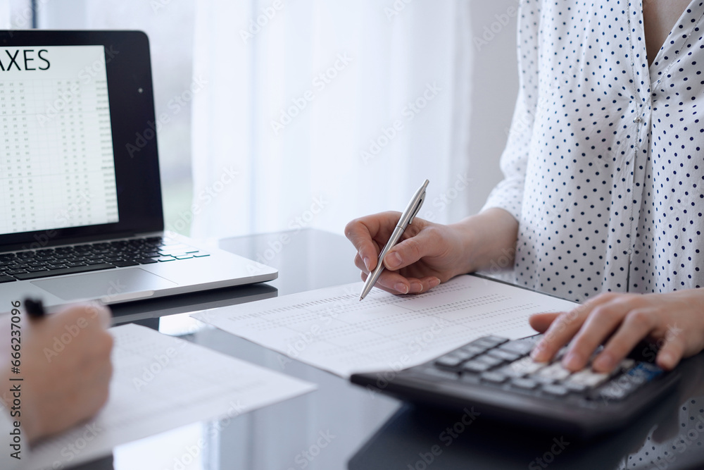 Two accountants use a calculator and laptop computer for counting taxes or revenue balance. Business, audit, and taxes concepts Two accountants use a calculator and laptop computer for counting taxes or revenue balance. Business, audit, and taxes concepts