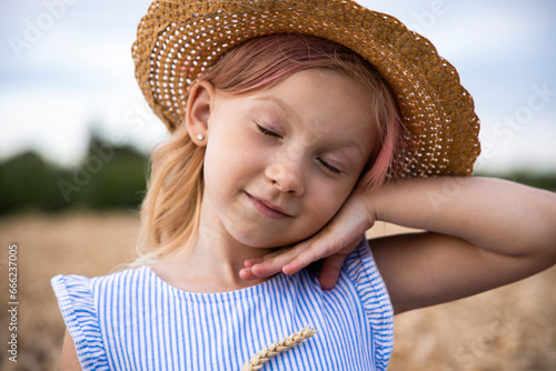 Child girl in a hat posing against the background of a wheat field