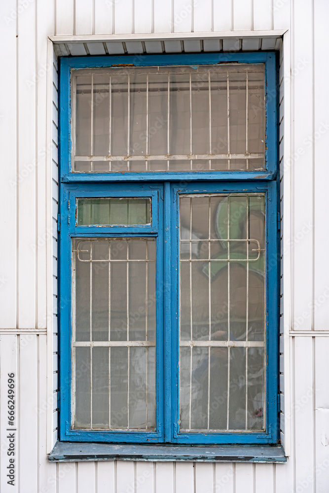 The wooden rectangular window is painted blue. With a metal grill on the glass.