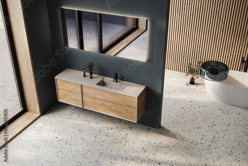 Comfortable bathtub and vanity with basin standing in modern bathroom dark blue and wooden walls and terrazzo floor photo