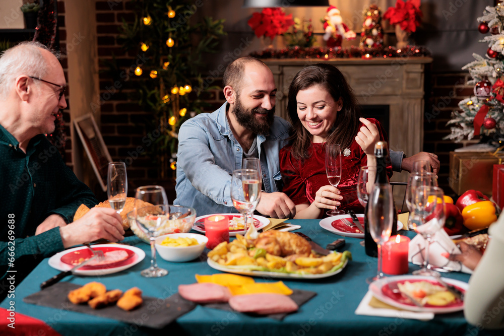 Cute couple meeting family at dinner on christmas eve holiday, gathering around table with persons to eat food and drink wine. Young adults talking to relatives during december event at home.