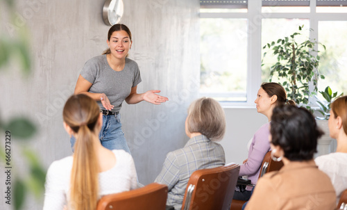 Canvas Print Emotional young female tutor leading educational class for group of women sitting in auditorium