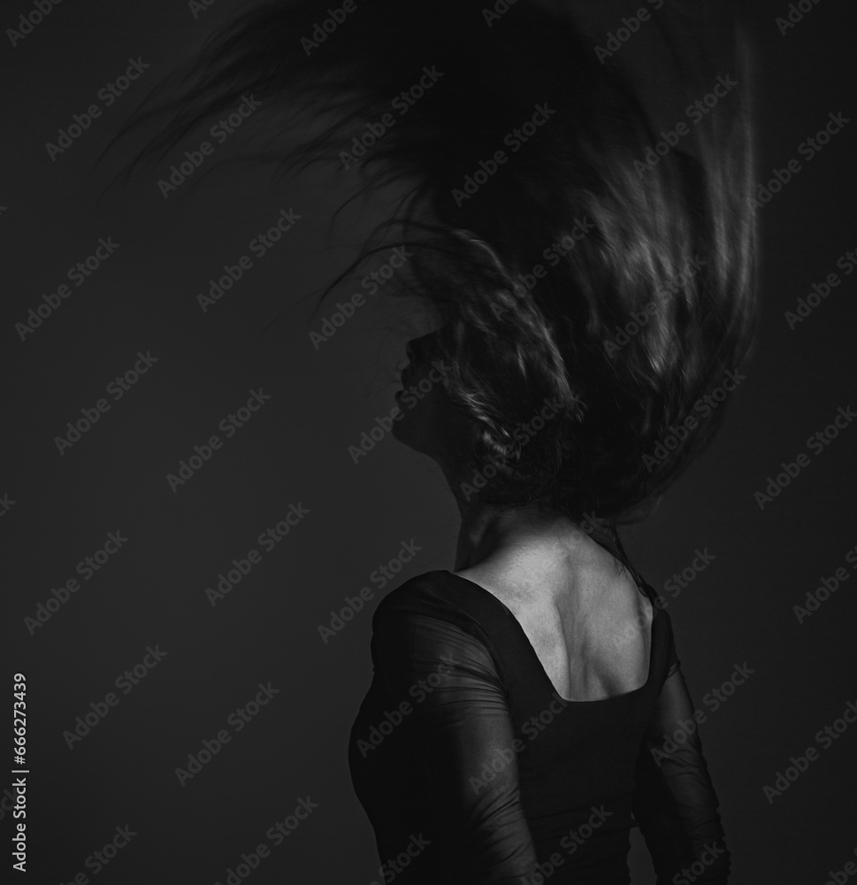 Silhouette of beautiful woman with sporty slim figure in black dress moving with hair above the head on dark shadow art background. Closeup