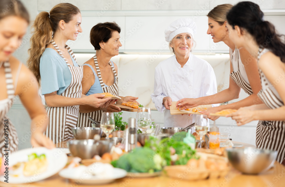 Elderly female chef teaches group of people how to cook chicken at master class