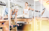 Positive mature woman practicing pilates stretching exercises on reformer at gym