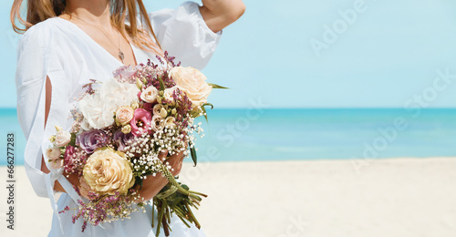 Obraz na płótnie Joyful Young Woman Holding a Bouquet of Flowers on a Beach with Blue Sky Background w salonie