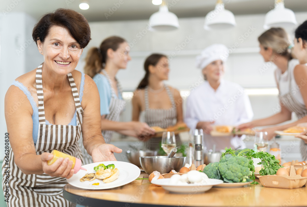 Mature lady visiting culinary school completes preparation of tender dietary poultry meat and puts small amount of spicy sauce on fillet