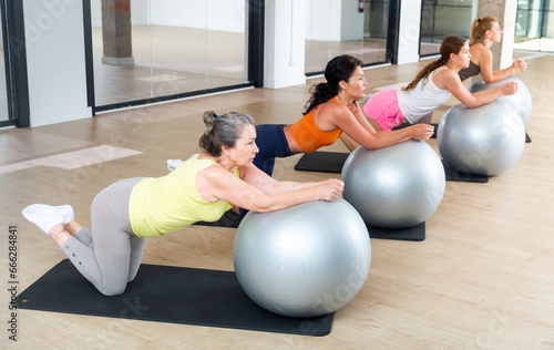 Women doing roll-out exercise with stability balls in fitness room
